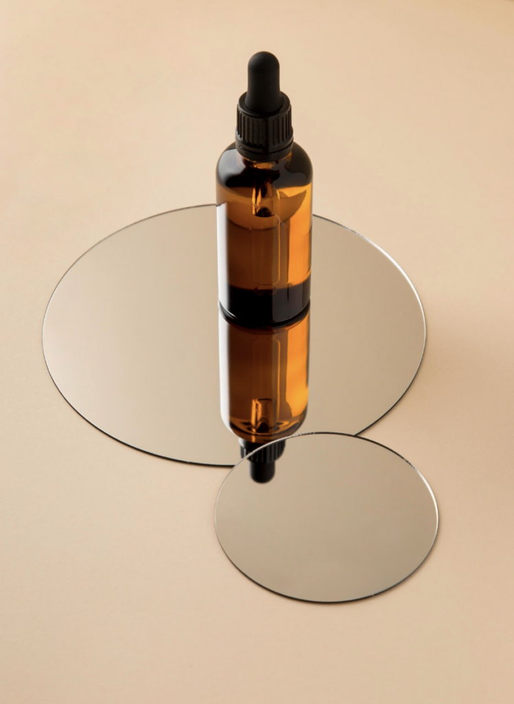 Solaire Intense Radiance Serum in een bruin glazen pipetflesje, staand op ronde spiegels voor een luxe uitstraling.